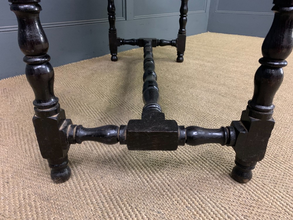 A dark carved oak side table featuring intricate lunette carvings, brass drop handles, three drawers, turned legs, and a stretcher base. View X