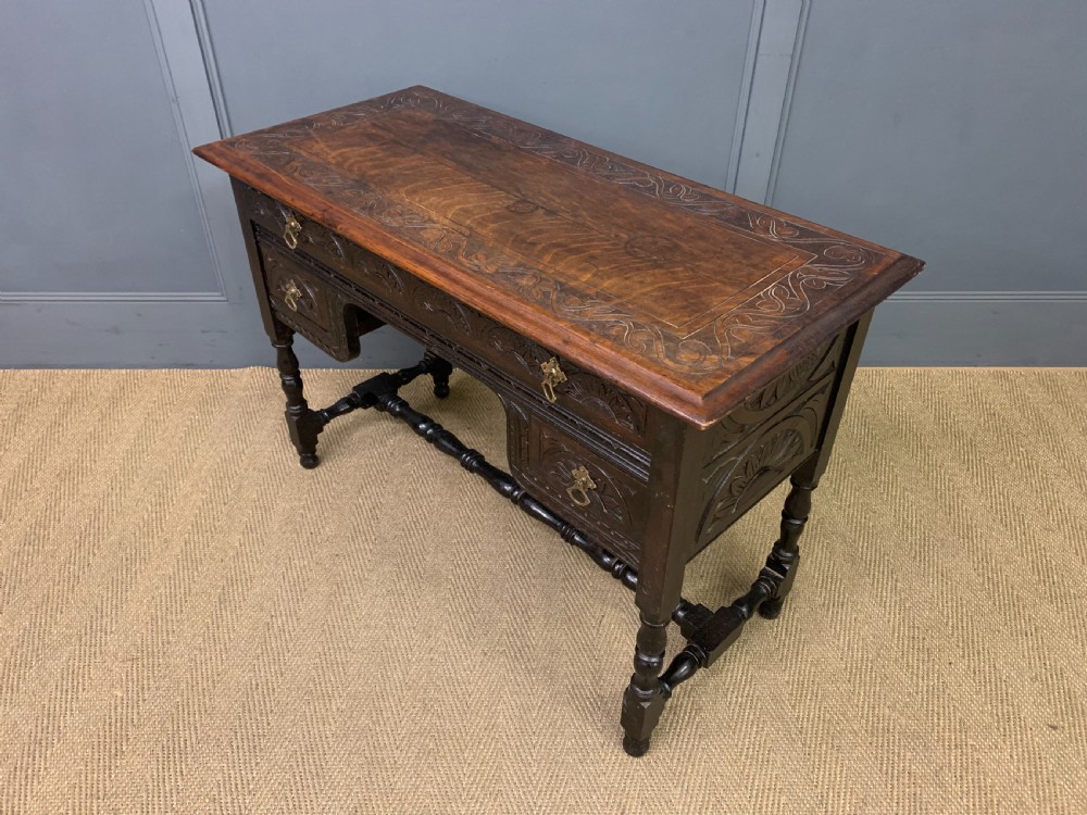 A dark carved oak side table featuring intricate lunette carvings, brass drop handles, three drawers, turned legs, and a stretcher base. View XIII