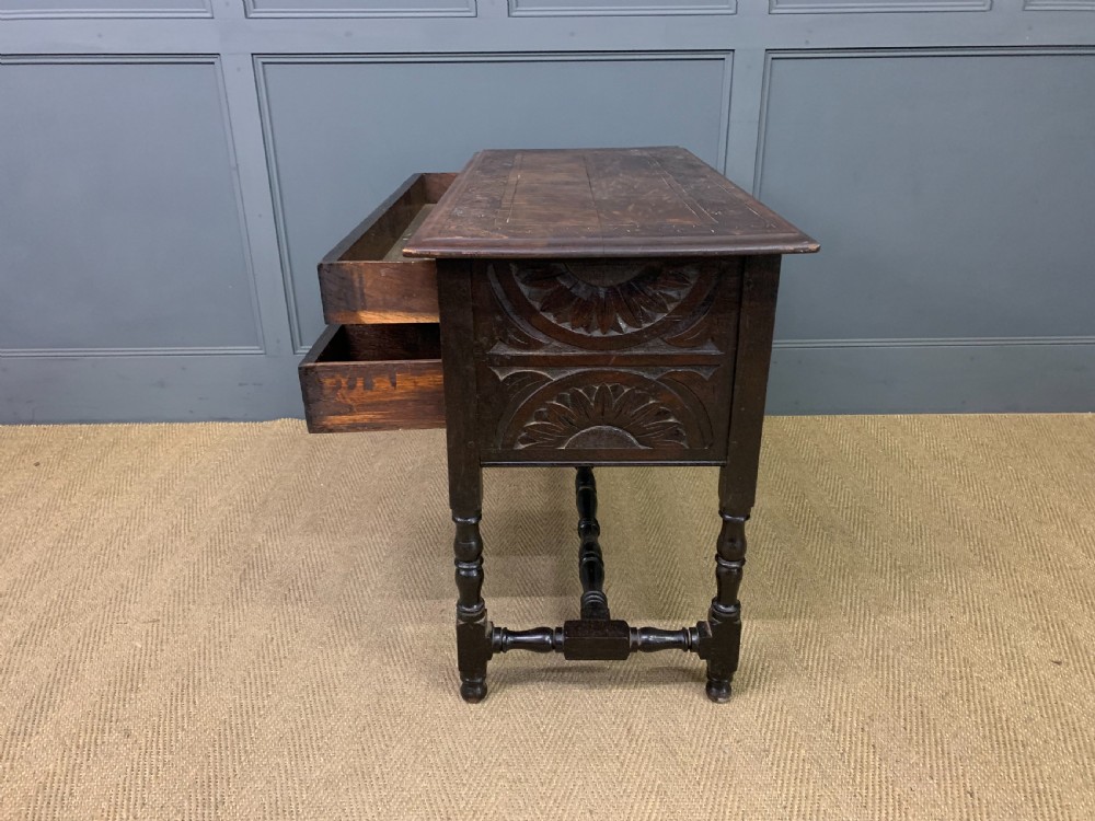 A dark carved oak side table featuring intricate lunette carvings, brass drop handles, three drawers, turned legs, and a stretcher base. View XIV