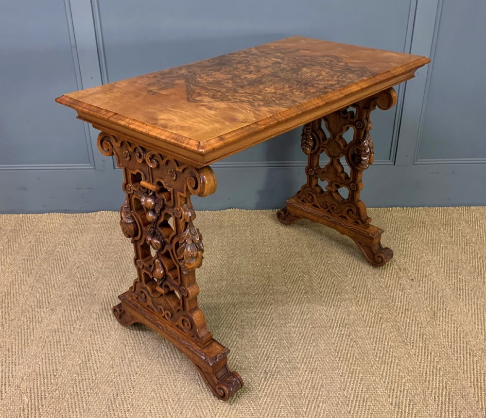 An antique Victorian rectangular table crafted from figured burr walnut veneer with intricately carved trestle supports.