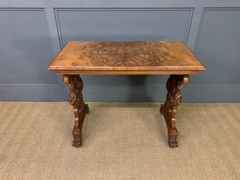 An antique Victorian rectangular table crafted from figured burr walnut veneer with intricately carved trestle supports. View II