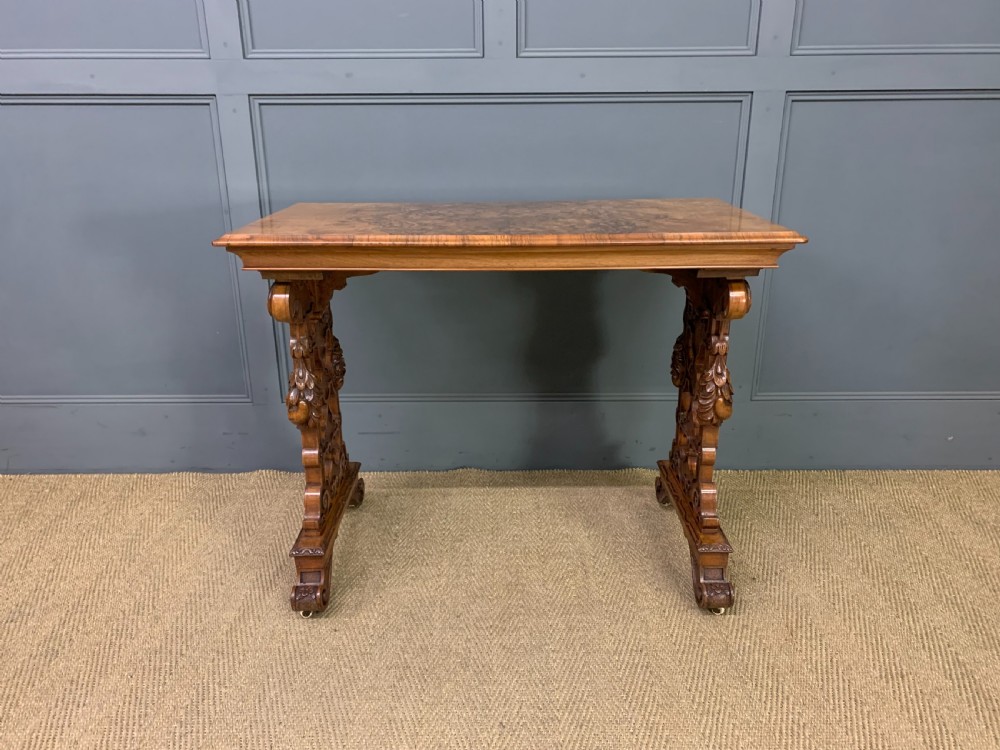 An antique Victorian rectangular table crafted from figured burr walnut veneer with intricately carved trestle supports. View III