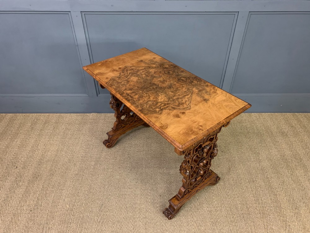 An antique Victorian rectangular table crafted from figured burr walnut veneer with intricately carved trestle supports. View X