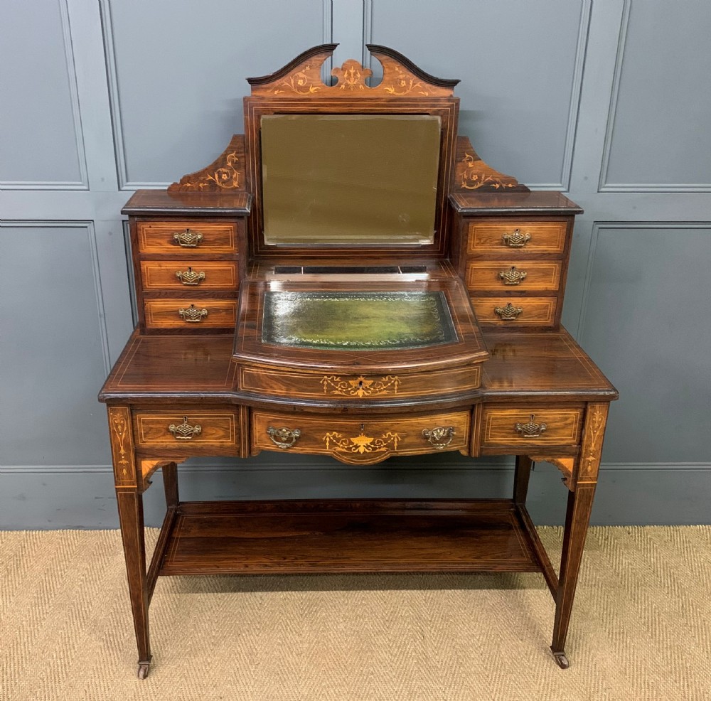 An antique rosewood bonheur du jour writing desk featuring intricate marquetry inlays, a central mirror, green leather writing top, and tapered legs on brass castors.