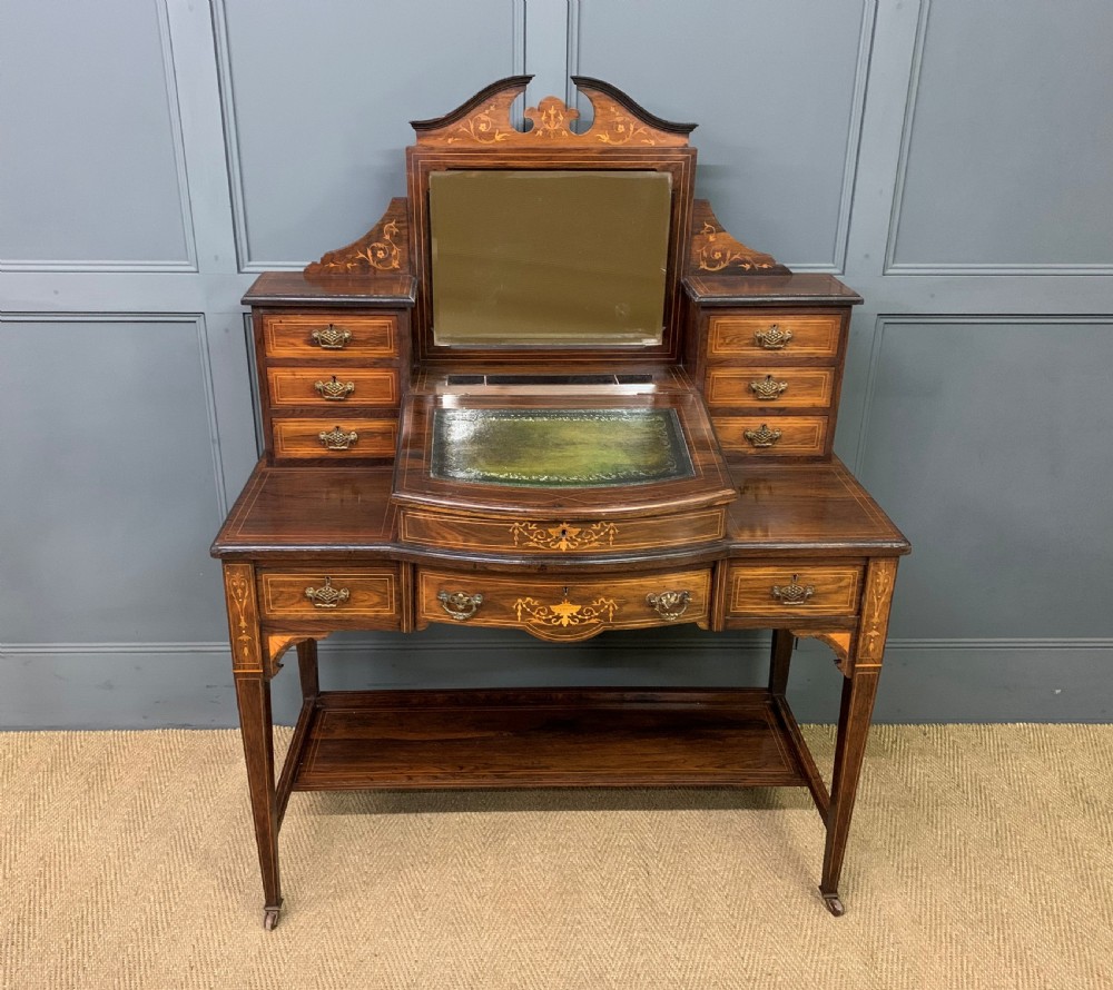 An antique rosewood bonheur du jour writing desk featuring intricate marquetry inlays, a central mirror, green leather writing top, and tapered legs on brass castors. View II