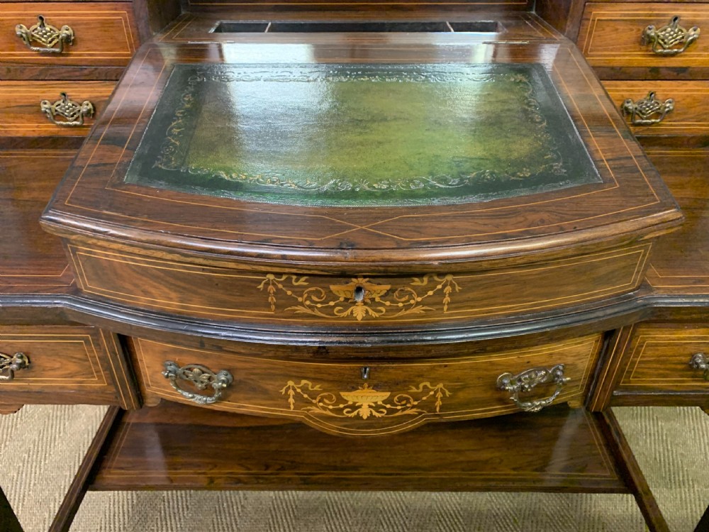 An antique rosewood bonheur du jour writing desk featuring intricate marquetry inlays, a central mirror, green leather writing top, and tapered legs on brass castors. View IV