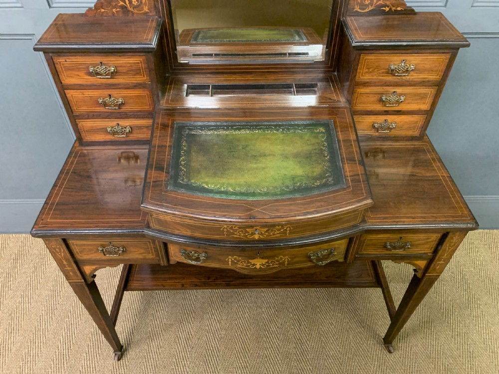 An antique rosewood bonheur du jour writing desk featuring intricate marquetry inlays, a central mirror, green leather writing top, and tapered legs on brass castors. View V