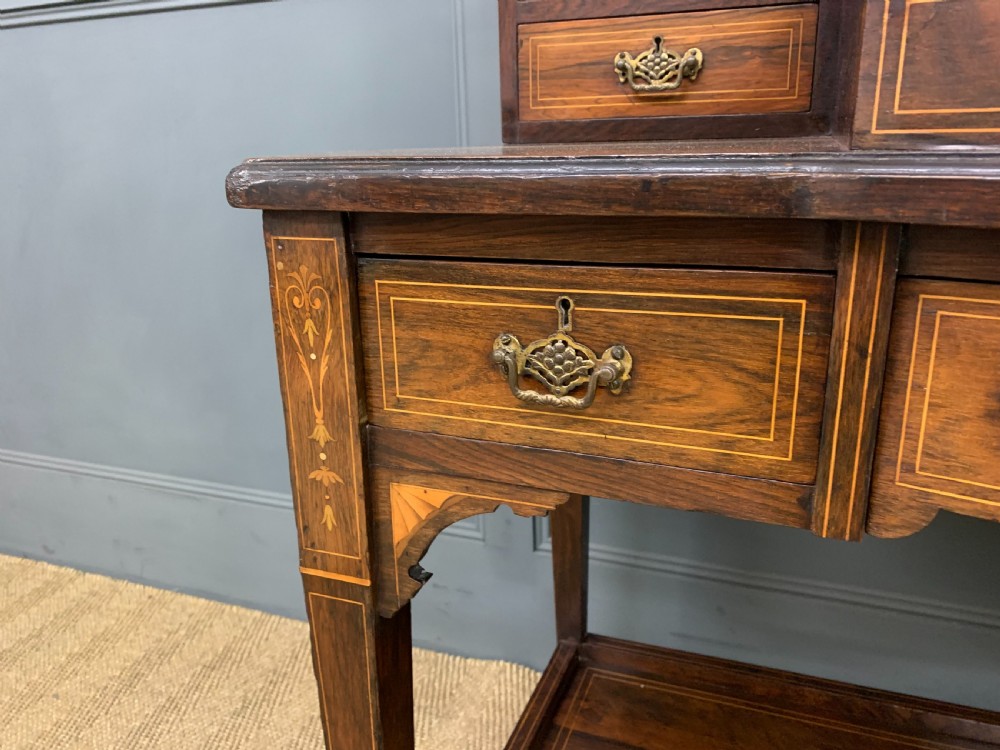 An antique rosewood bonheur du jour writing desk featuring intricate marquetry inlays, a central mirror, green leather writing top, and tapered legs on brass castors. View VII