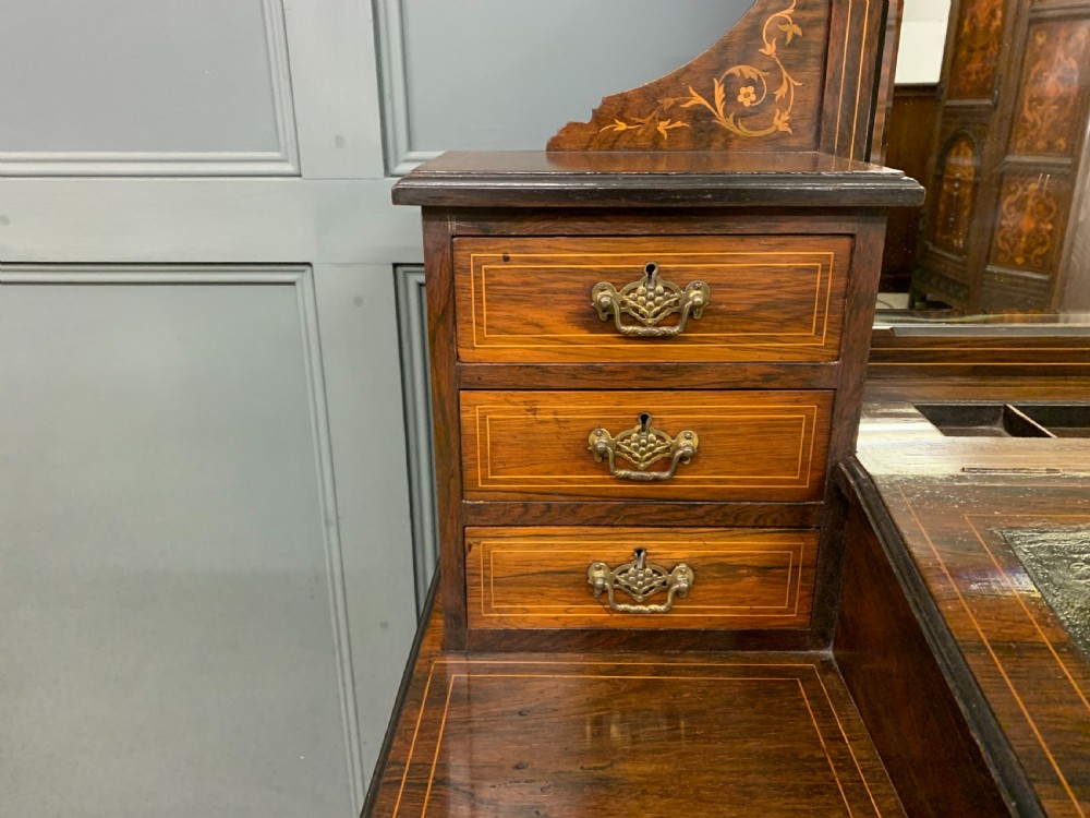 An antique rosewood bonheur du jour writing desk featuring intricate marquetry inlays, a central mirror, green leather writing top, and tapered legs on brass castors. View VIII