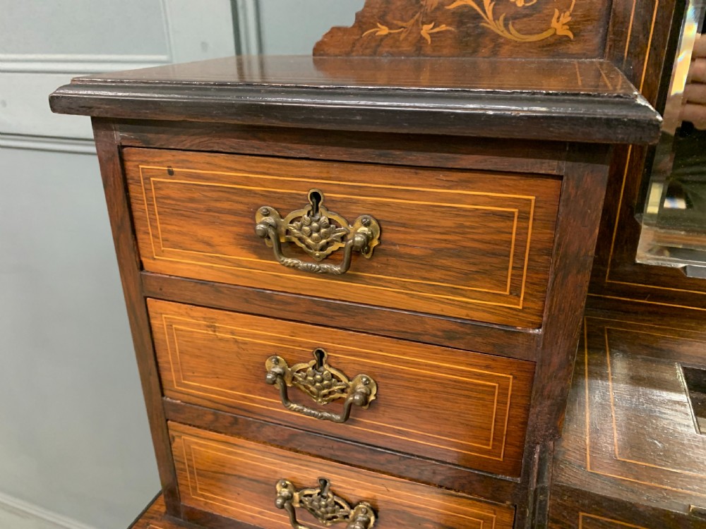 An antique rosewood bonheur du jour writing desk featuring intricate marquetry inlays, a central mirror, green leather writing top, and tapered legs on brass castors. View IX