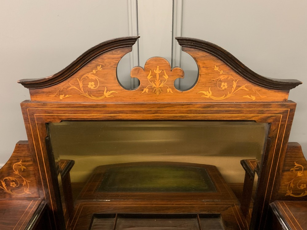 An antique rosewood bonheur du jour writing desk featuring intricate marquetry inlays, a central mirror, green leather writing top, and tapered legs on brass castors. View X