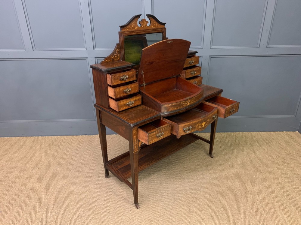 An antique rosewood bonheur du jour writing desk featuring intricate marquetry inlays, a central mirror, green leather writing top, and tapered legs on brass castors. View XIII
