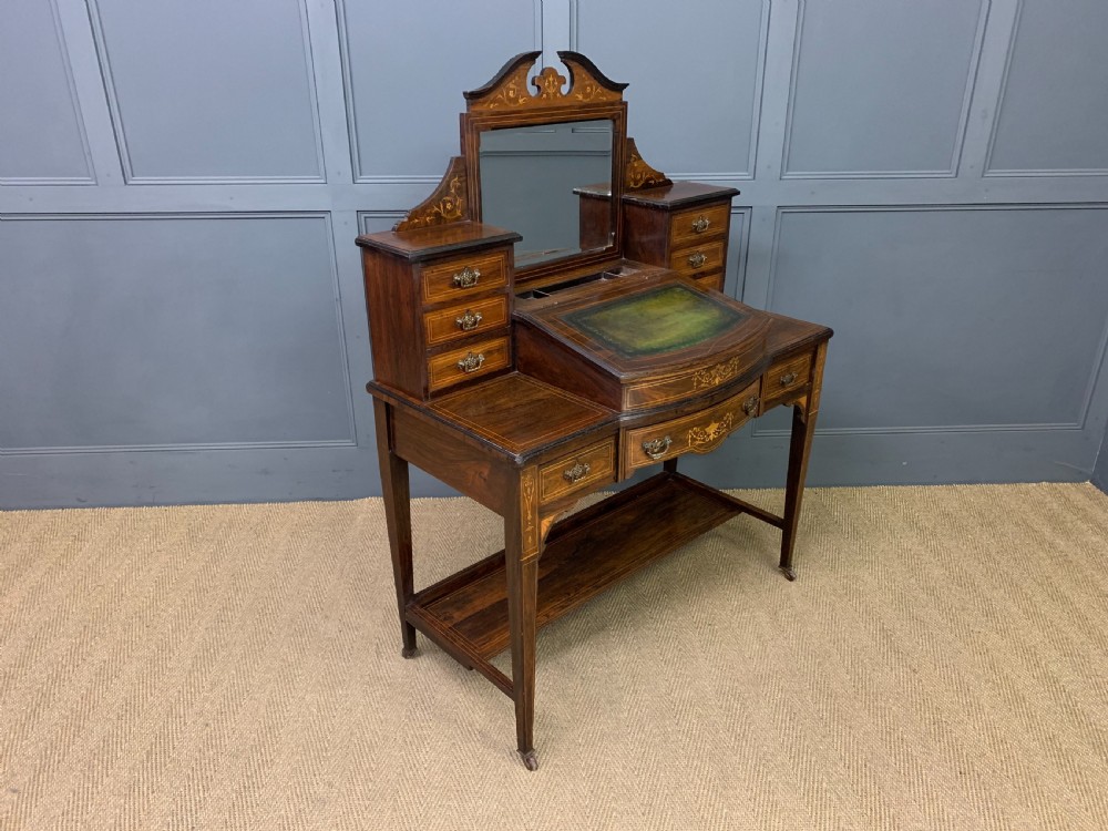 An antique rosewood bonheur du jour writing desk featuring intricate marquetry inlays, a central mirror, green leather writing top, and tapered legs on brass castors. View XV