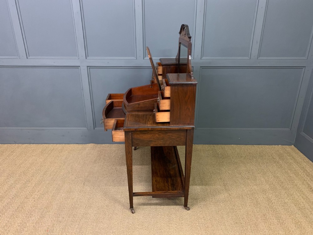 An antique rosewood bonheur du jour writing desk featuring intricate marquetry inlays, a central mirror, green leather writing top, and tapered legs on brass castors. View XVII