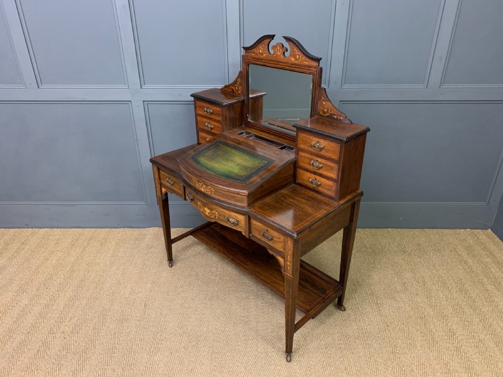 An antique rosewood bonheur du jour writing desk featuring intricate marquetry inlays, a central mirror, green leather writing top, and tapered legs on brass castors. View XIX