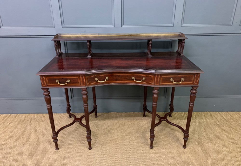 A late Victorian mahogany writing desk by Collinson and Lock with a raised upper shelf gallery, leather top, satinwood inlay, and turned legs.