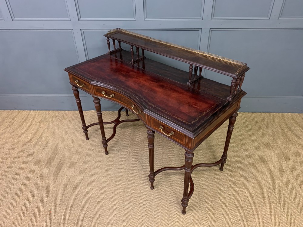 A late Victorian mahogany writing desk by Collinson and Lock with a raised upper shelf gallery, leather top, satinwood inlay, and turned legs. View XVI