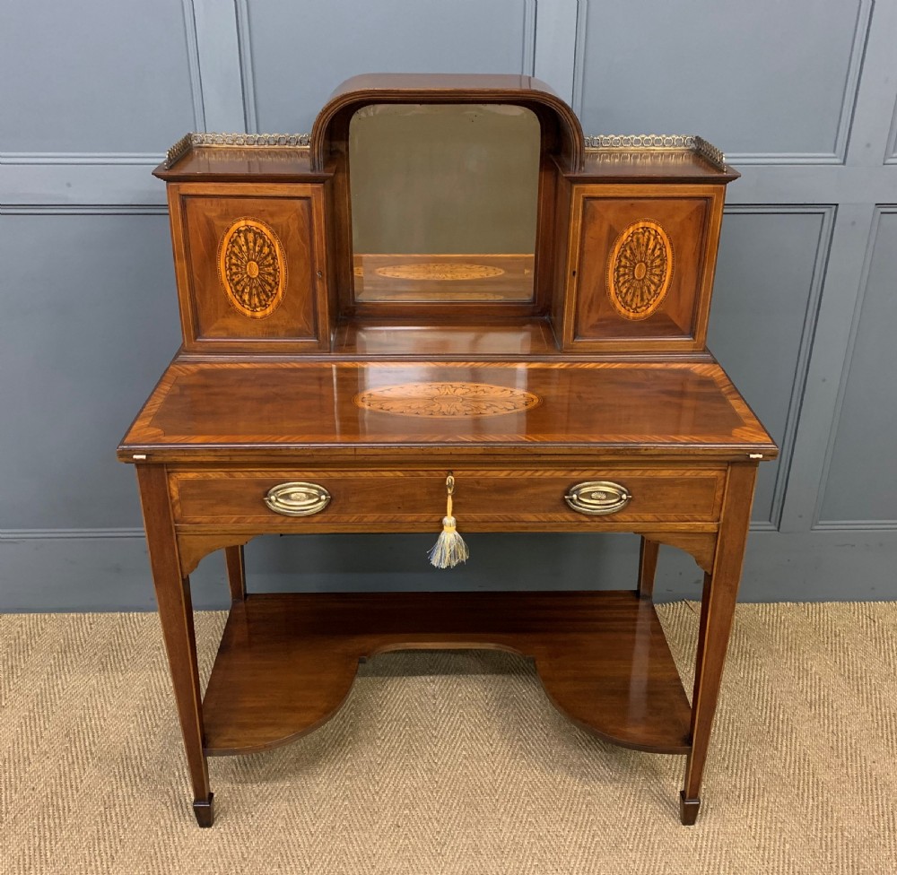 An Edwardian inlaid mahogany bonheur du jour writing desk featuring a central arched mirror, twin side cabinets with oval marquetry, brass galleries, and a lower shelf over tapered legs.