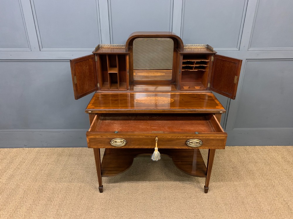 An Edwardian inlaid mahogany bonheur du jour writing desk featuring a central arched mirror, twin side cabinets with oval marquetry, brass galleries, and a lower shelf over tapered legs. View IV