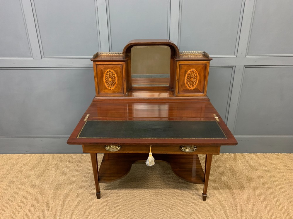 An Edwardian inlaid mahogany bonheur du jour writing desk featuring a central arched mirror, twin side cabinets with oval marquetry, brass galleries, and a lower shelf over tapered legs. View V