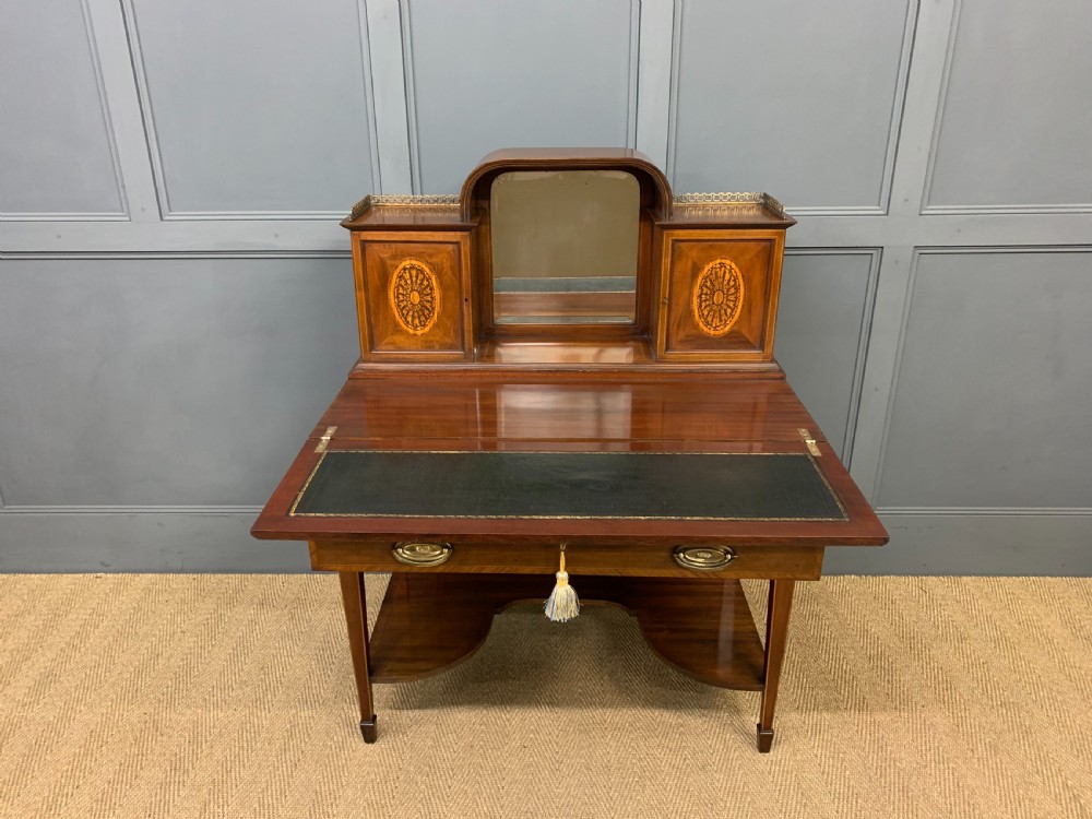 An Edwardian inlaid mahogany bonheur du jour writing desk featuring a central arched mirror, twin side cabinets with oval marquetry, brass galleries, and a lower shelf over tapered legs. View VI