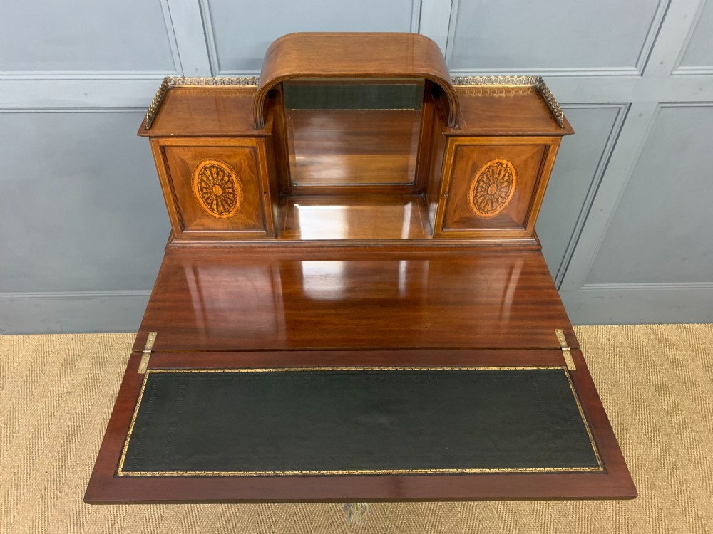 An Edwardian inlaid mahogany bonheur du jour writing desk featuring a central arched mirror, twin side cabinets with oval marquetry, brass galleries, and a lower shelf over tapered legs. View VII
