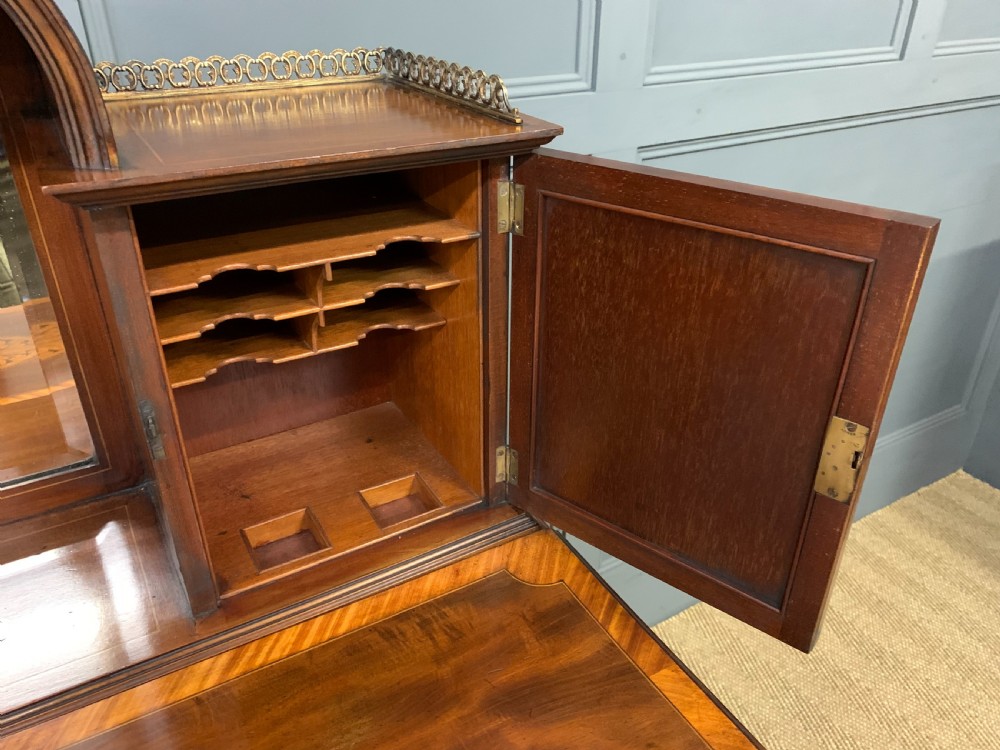An Edwardian inlaid mahogany bonheur du jour writing desk featuring a central arched mirror, twin side cabinets with oval marquetry, brass galleries, and a lower shelf over tapered legs. View XVII
