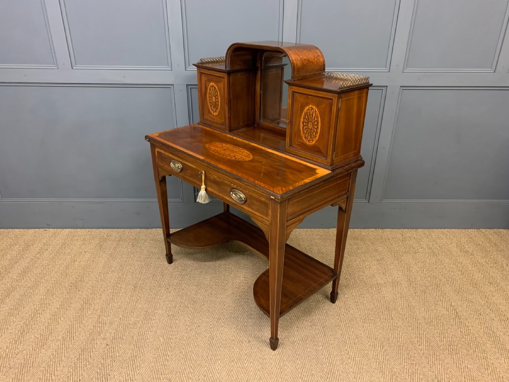 An Edwardian inlaid mahogany bonheur du jour writing desk featuring a central arched mirror, twin side cabinets with oval marquetry, brass galleries, and a lower shelf over tapered legs. View XVIII