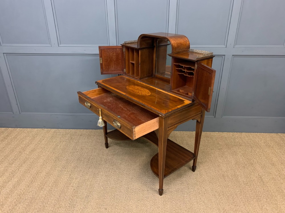 An Edwardian inlaid mahogany bonheur du jour writing desk featuring a central arched mirror, twin side cabinets with oval marquetry, brass galleries, and a lower shelf over tapered legs. View XX