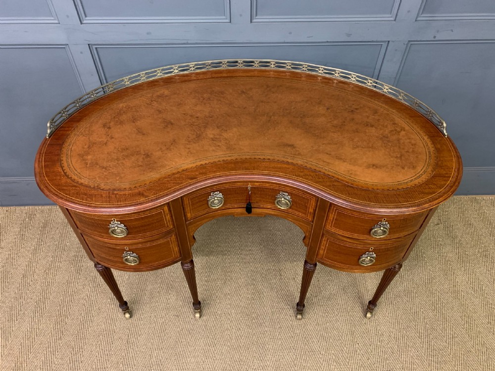 An Edwardian kidney-shaped mahogany writing desk featuring satinwood inlay, a leather writing surface, a brass gallery rail, and five drawers on fluted legs. View III