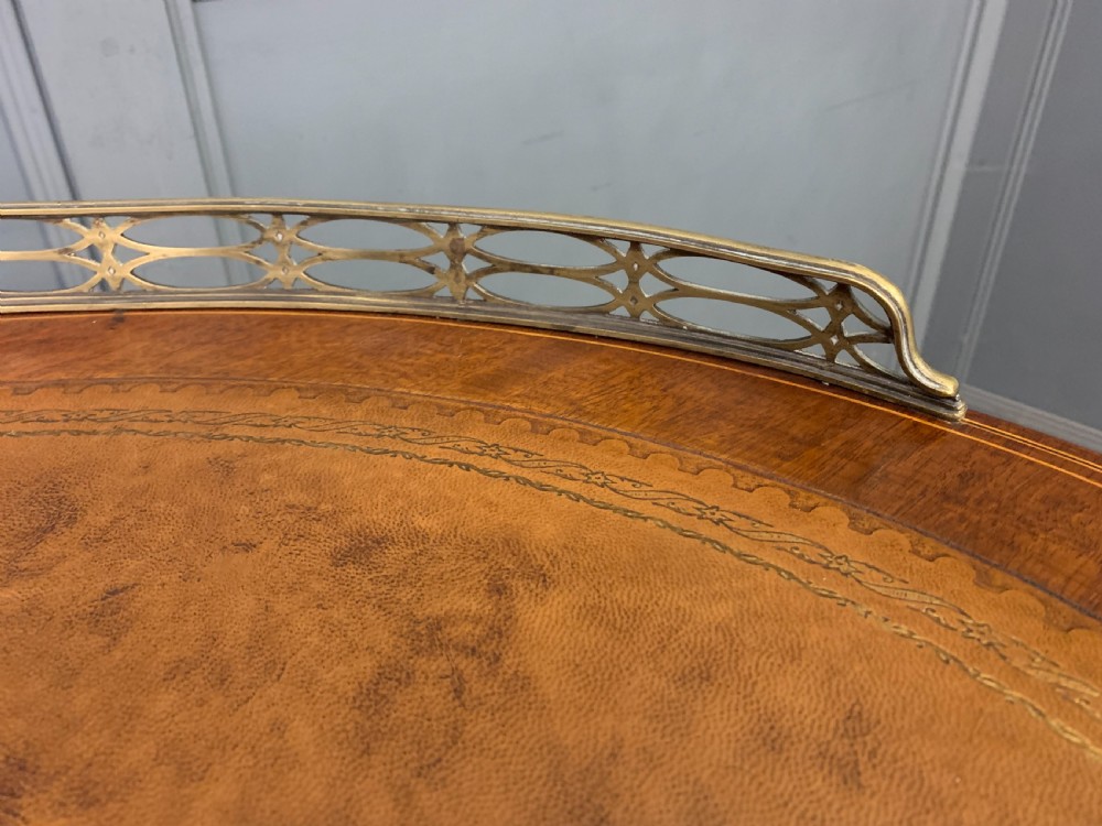 An Edwardian kidney-shaped mahogany writing desk featuring satinwood inlay, a leather writing surface, a brass gallery rail, and five drawers on fluted legs. View IV