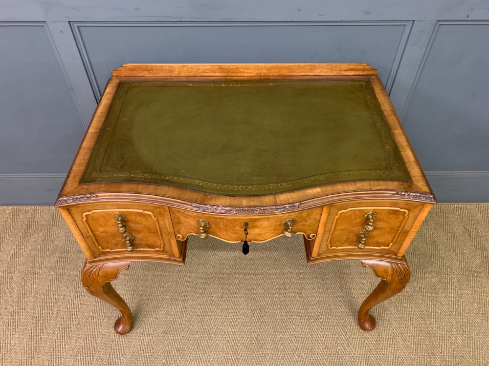 A Queen Anne style burr walnut writing desk with an inset green leather surface, five drawers, brass drop pulls, and carved cabriole legs. View III