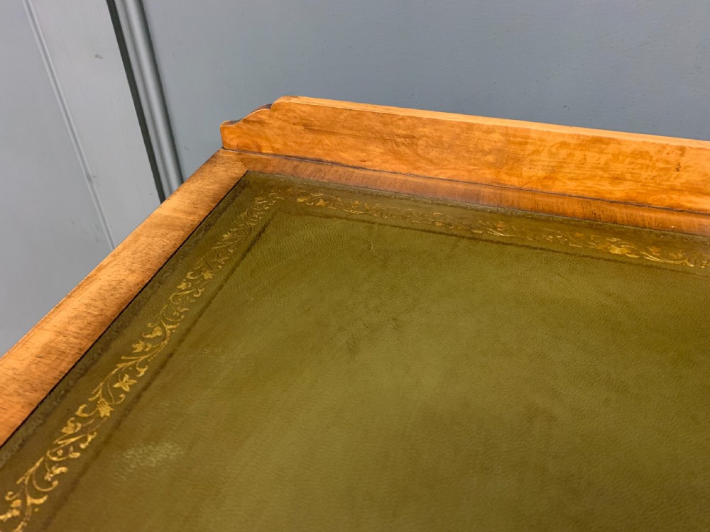 A Queen Anne style burr walnut writing desk with an inset green leather surface, five drawers, brass drop pulls, and carved cabriole legs. View V