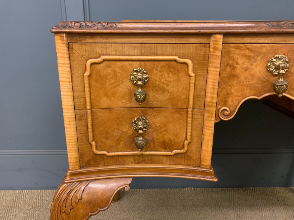 A Queen Anne style burr walnut writing desk with an inset green leather surface, five drawers, brass drop pulls, and carved cabriole legs. View VI