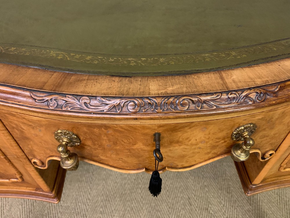 A Queen Anne style burr walnut writing desk with an inset green leather surface, five drawers, brass drop pulls, and carved cabriole legs. View VIII