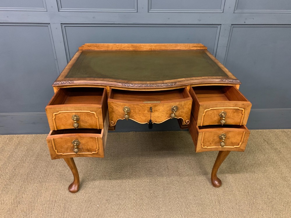 A Queen Anne style burr walnut writing desk with an inset green leather surface, five drawers, brass drop pulls, and carved cabriole legs. View IX