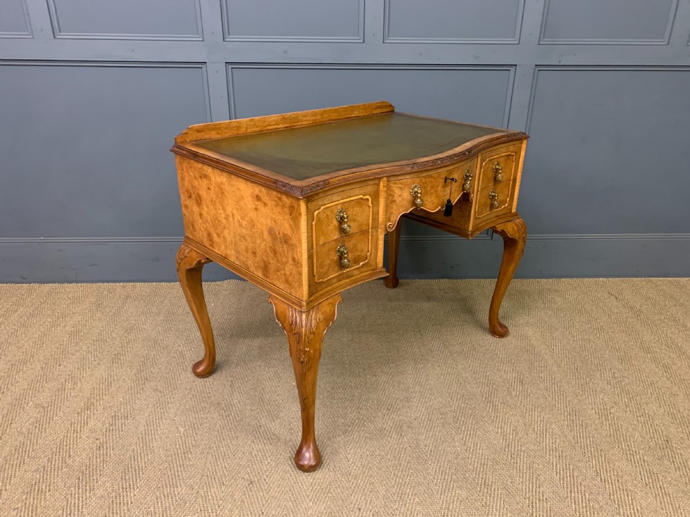 A Queen Anne style burr walnut writing desk with an inset green leather surface, five drawers, brass drop pulls, and carved cabriole legs. View X