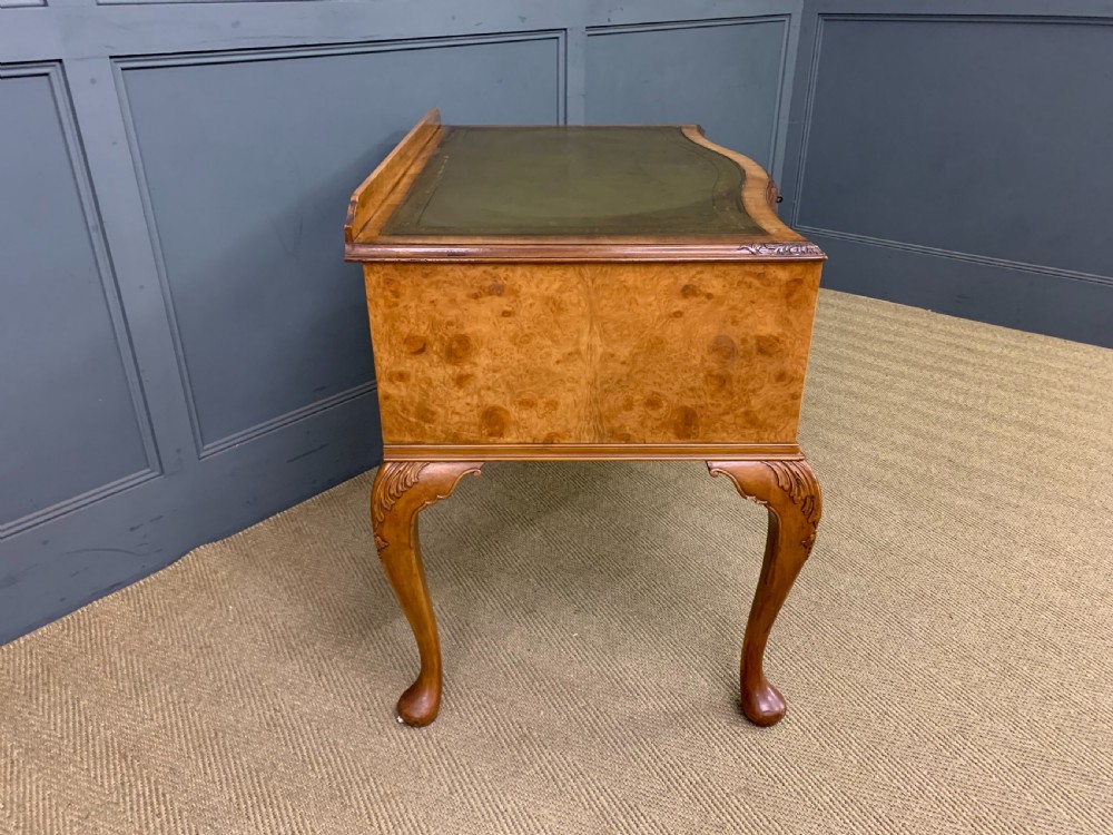 A Queen Anne style burr walnut writing desk with an inset green leather surface, five drawers, brass drop pulls, and carved cabriole legs. View XI
