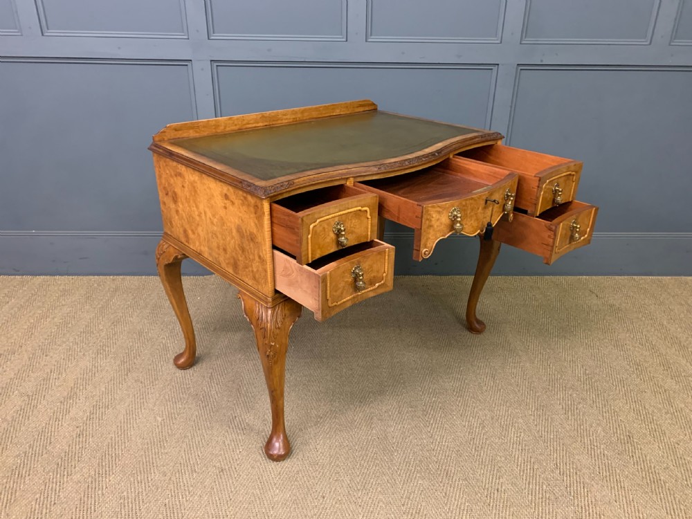 A Queen Anne style burr walnut writing desk with an inset green leather surface, five drawers, brass drop pulls, and carved cabriole legs. View XII
