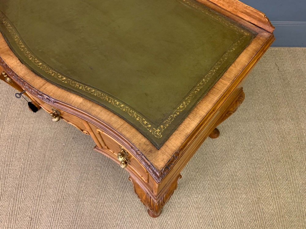 A Queen Anne style burr walnut writing desk with an inset green leather surface, five drawers, brass drop pulls, and carved cabriole legs. View XIV