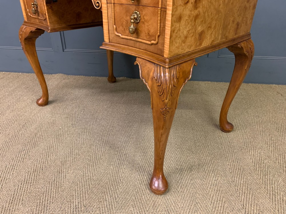 A Queen Anne style burr walnut writing desk with an inset green leather surface, five drawers, brass drop pulls, and carved cabriole legs. View XV