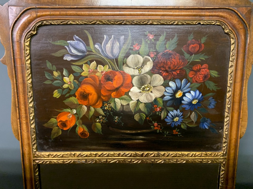 A vertical Queen Anne Revival walnut wall mirror featuring a scroll-cut frame, a gilded carved shell at the top crest, and a hand-painted floral still-life panel above the reflective mirror glass. View V