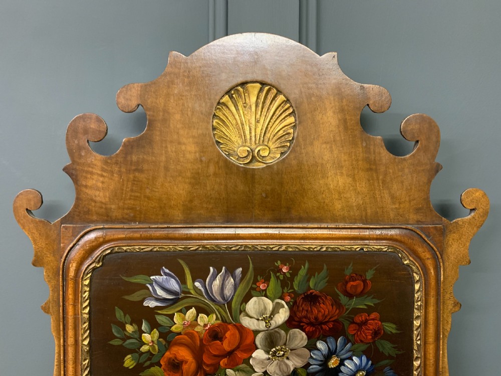 A vertical Queen Anne Revival walnut wall mirror featuring a scroll-cut frame, a gilded carved shell at the top crest, and a hand-painted floral still-life panel above the reflective mirror glass. View VI