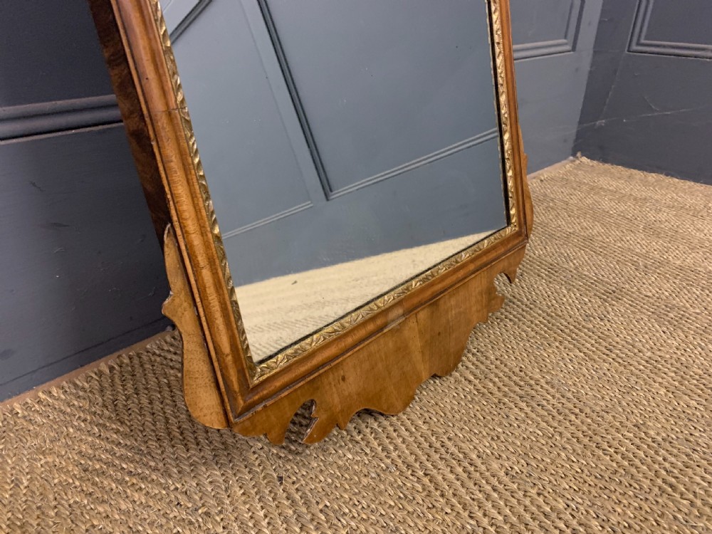 A vertical Queen Anne Revival walnut wall mirror featuring a scroll-cut frame, a gilded carved shell at the top crest, and a hand-painted floral still-life panel above the reflective mirror glass. View VII