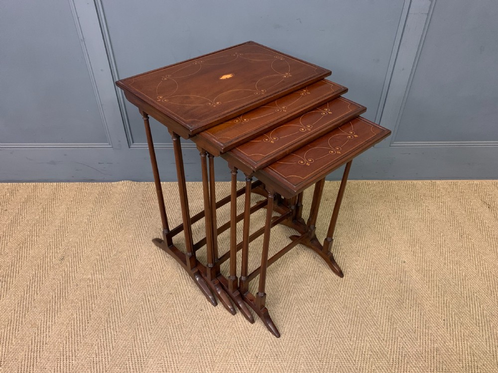A set of four graduating mahogany nest of tables featuring satinwood line inlay and slender turned legs.