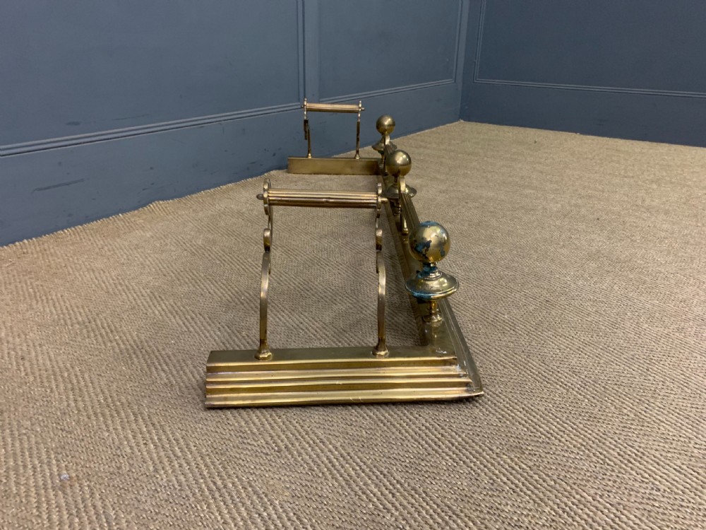 A Victorian brass fireplace fender featuring decorative finials and scrollwork rests, shown with three matching brass fire tools including a shovel, tongs, and poker. View VIII