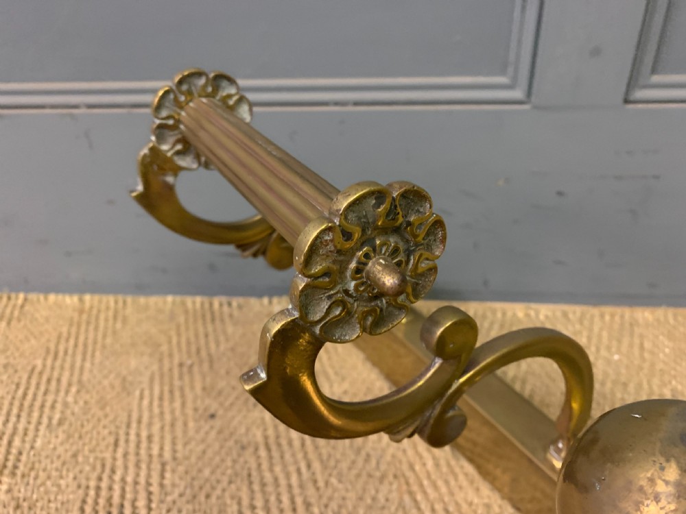 A Victorian brass fireplace fender featuring decorative finials and scrollwork rests, shown with three matching brass fire tools including a shovel, tongs, and poker. View X