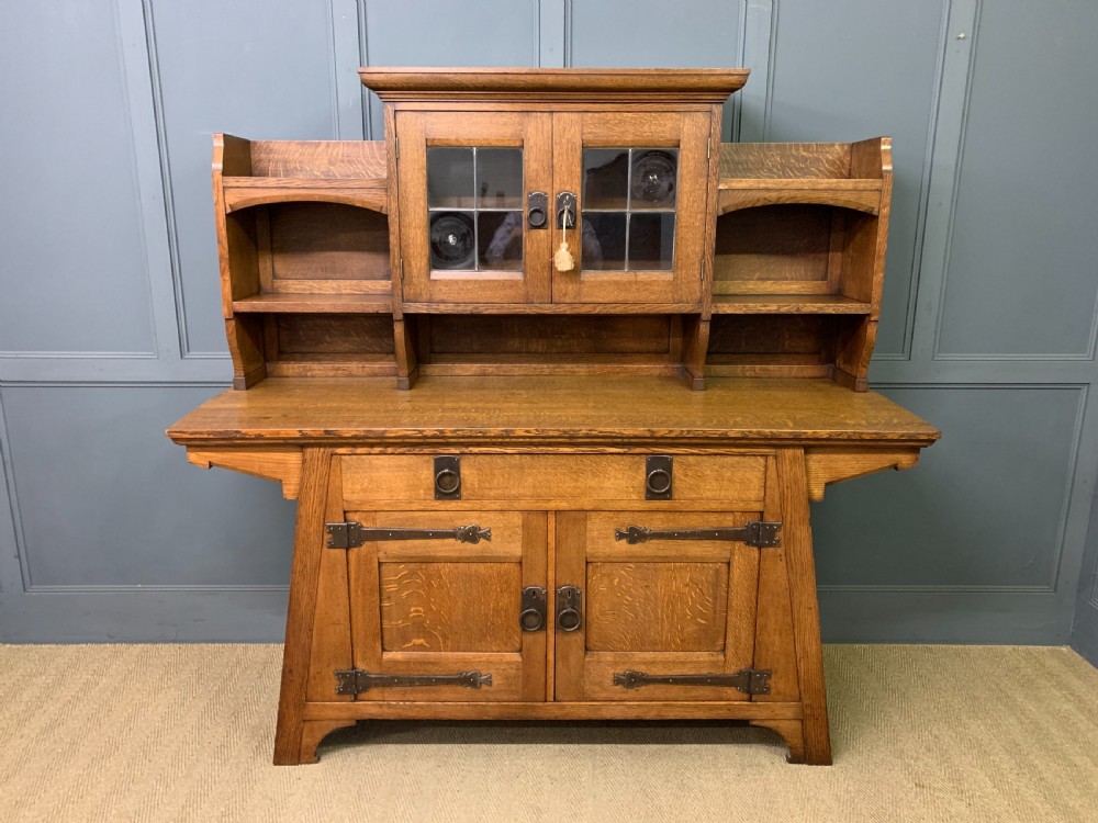 An Arts and Crafts period oak dresser featuring leaded glass upper cabinet doors, open side shelves, metal strap hinges, and a lower two-door cupboard. View II