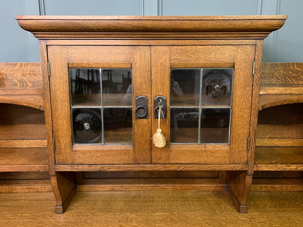 An Arts and Crafts period oak dresser featuring leaded glass upper cabinet doors, open side shelves, metal strap hinges, and a lower two-door cupboard. View III