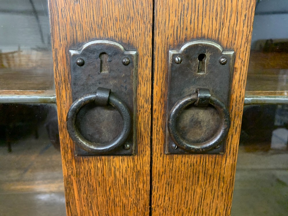 An Arts and Crafts period oak dresser featuring leaded glass upper cabinet doors, open side shelves, metal strap hinges, and a lower two-door cupboard. View V